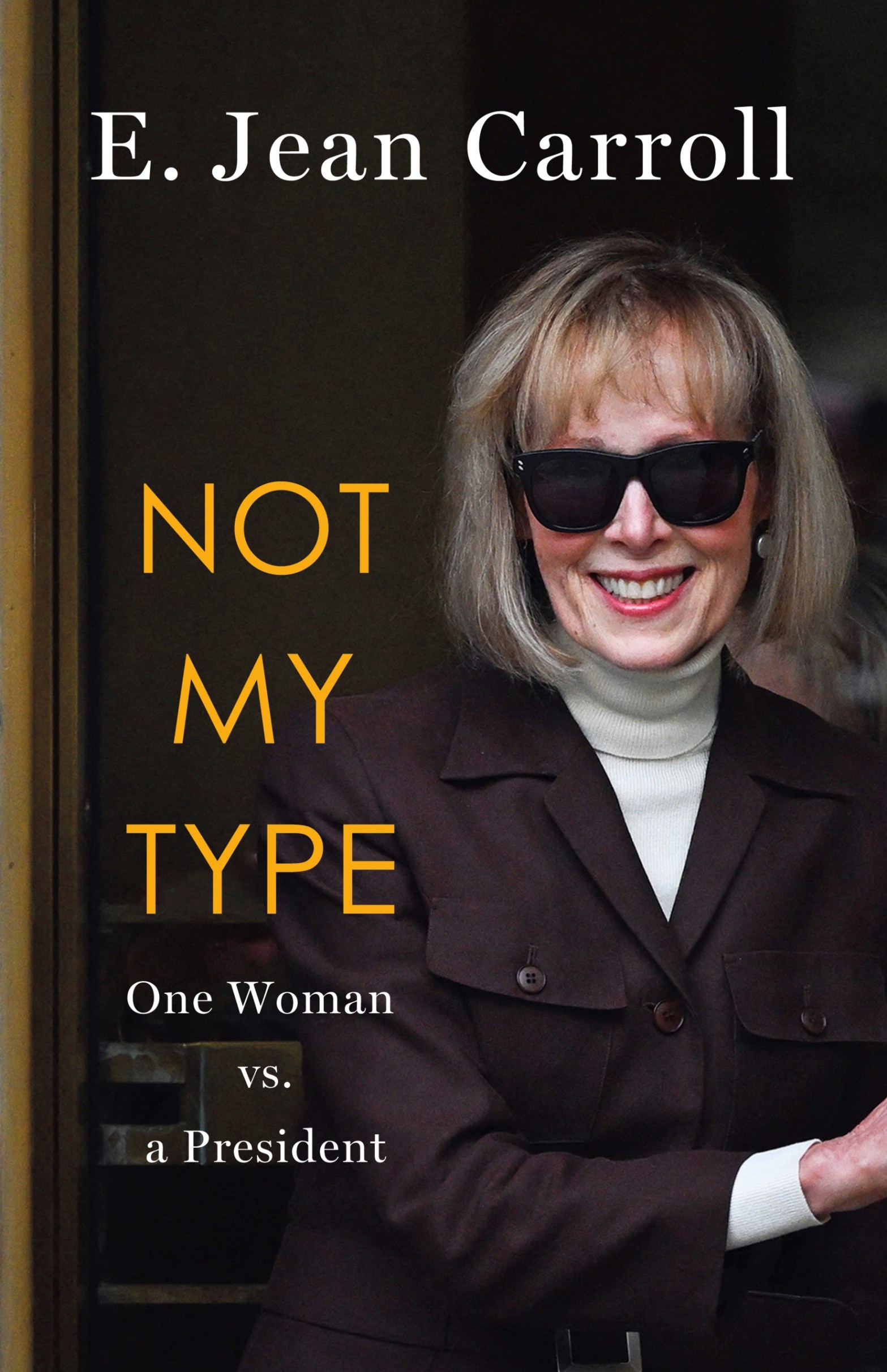 Book cover for Not My Type by E. Jean Carroll, featuring the author, a white woman with a blonde bob, wearing a white turtleneck and black blazer, crossing her arms and smiling. She's wearing dark sunglasses.